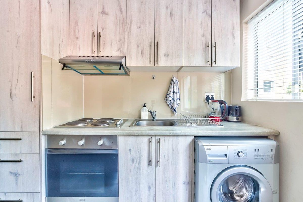 Compact kitchen featuring light wood-grain cabinetry, stainless steel appliances, integrated oven and hob, and a glass splashback with a functional sink area.