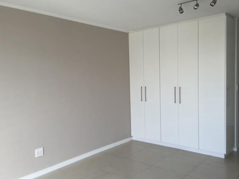 A clean, empty bedroom featuring modern white built-in cupboards, neutral wall tones, and tiled flooring with contemporary track lighting.