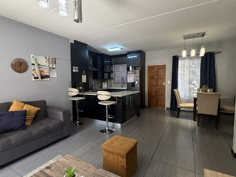 Open-plan living and dining area featuring a modern kitchen with dark cabinetry, stone countertops, and tiled flooring throughout.