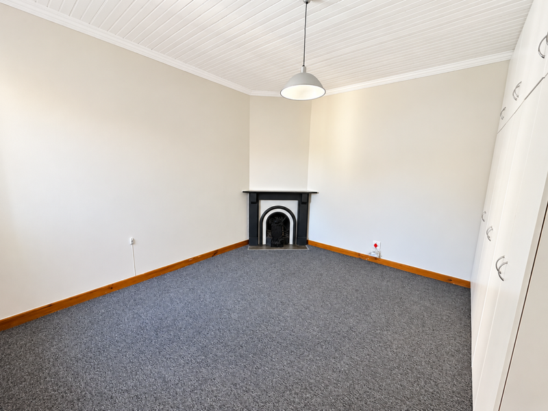 A bright, empty bedroom featuring a classic fireplace, built-in cupboards, and neutral carpeting, offering a clean and versatile space.