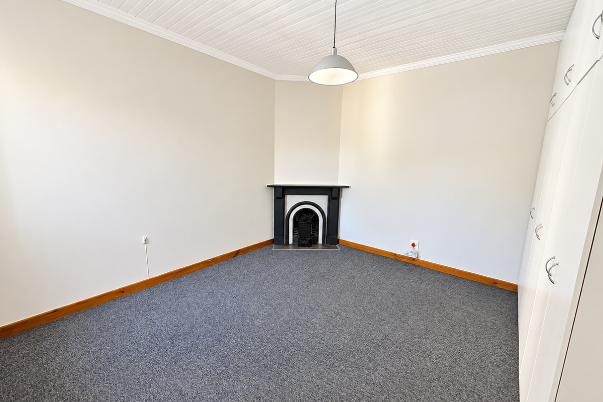 A bright, empty bedroom featuring a classic fireplace, built-in cupboards, and neutral carpeting, offering a clean and versatile space.
