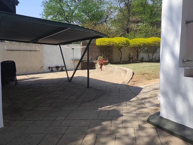A paved outdoor patio area featuring a covered carport structure, retaining wall, and a private garden space with boundary walling.