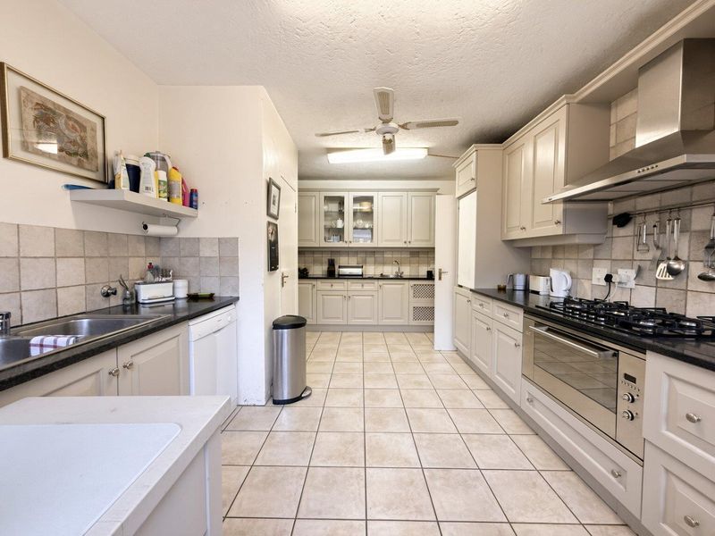 A functional kitchen featuring built-in cabinetry, a gas hob with extractor fan, tiled backsplash, and tiled flooring throughout.