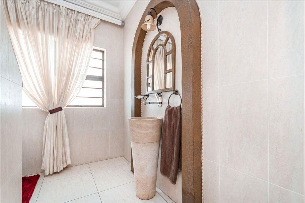 A well-maintained bathroom featuring a unique stone pedestal basin set within a decorative arched wall niche and neutral floor-to-ceiling tiling.