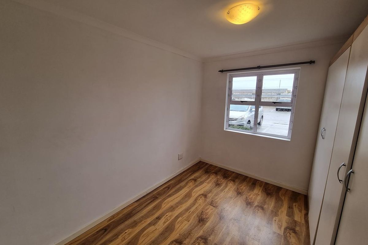 A clean, empty bedroom featuring wood-look laminate flooring, a built-in wardrobe, and a window providing natural light.