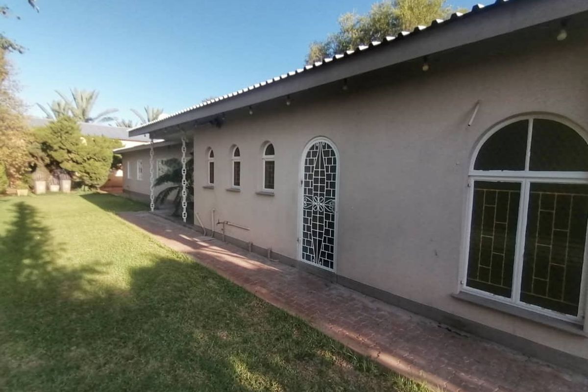 Rear view of the property featuring a paved walkway, arched windows with security bars, and a security gate leading to the garden area.