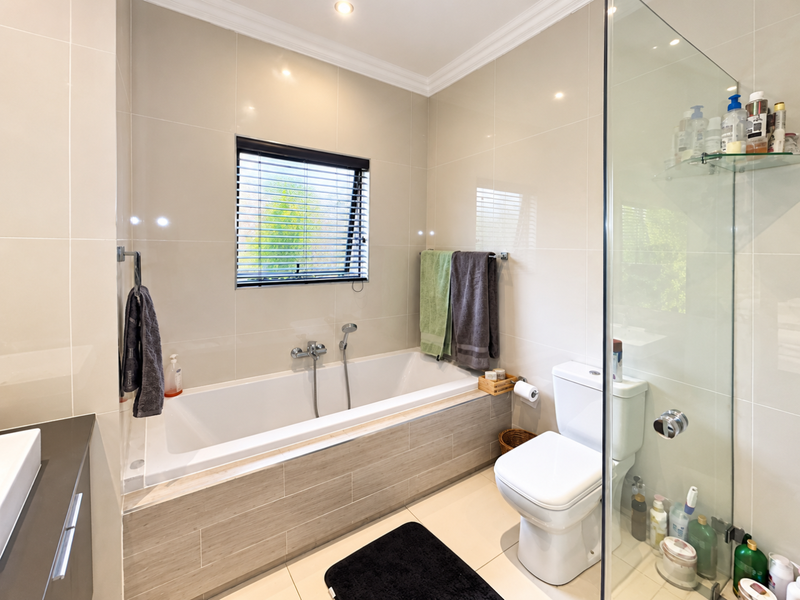 Modern bathroom featuring a built-in bathtub, separate glass-enclosed shower, tiled finishes, and neutral decor, offering a clean and functional space.