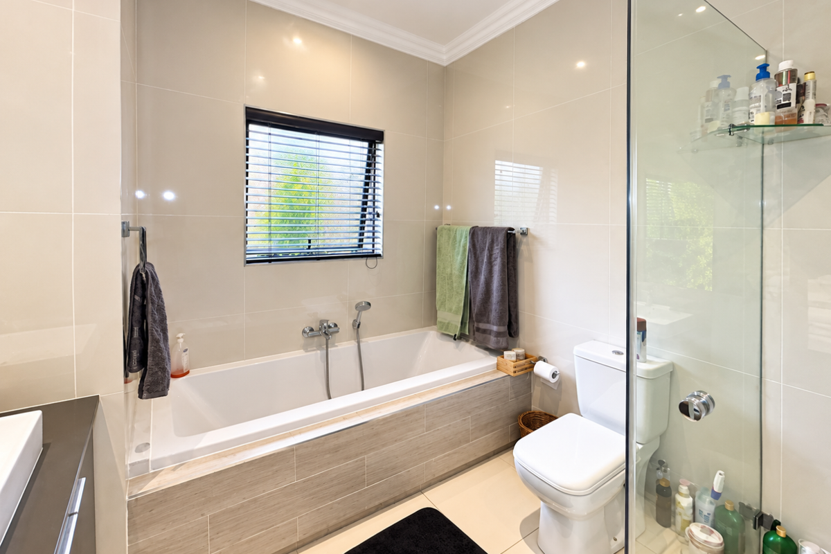 Modern bathroom featuring a built-in bathtub, separate glass-enclosed shower, tiled finishes, and neutral decor, offering a clean and functional space.