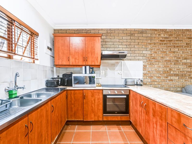 A functional kitchen featuring wooden cabinetry, laminate countertops, a built-in oven with hob, and a distinctive exposed brick feature wall.