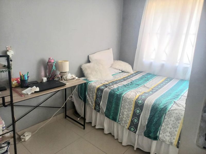A compact bedroom featuring tiled flooring and a window fitted with security bars, providing natural light.