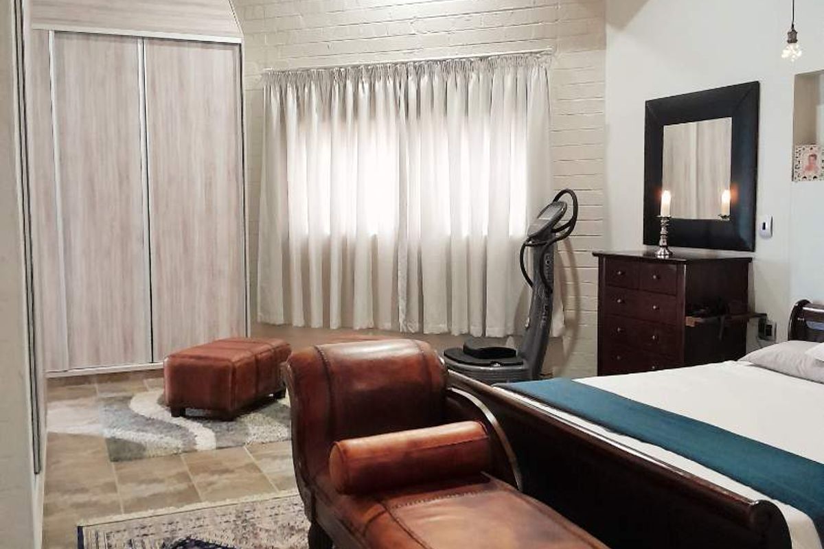 Spacious bedroom featuring high vaulted timber ceilings, exposed brickwork, and built-in sliding door wardrobes with tiled flooring.