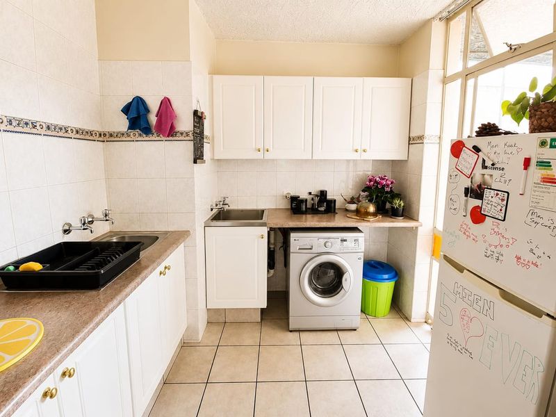 A functional laundry area featuring built-in white cabinetry, laminate countertops, a stainless steel sink, and tiled finishes throughout.