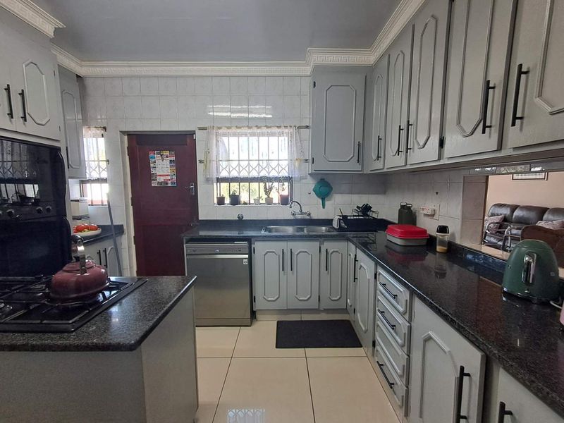 A functional kitchen featuring granite countertops, built-in cabinetry, a gas hob, and tiled flooring with a classic layout.