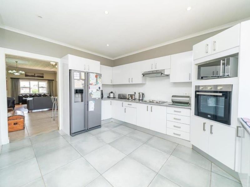 Modern kitchen featuring white cabinetry, built-in oven and microwave, extractor fan, and tiled flooring, with an open flow into the adjacent living area.