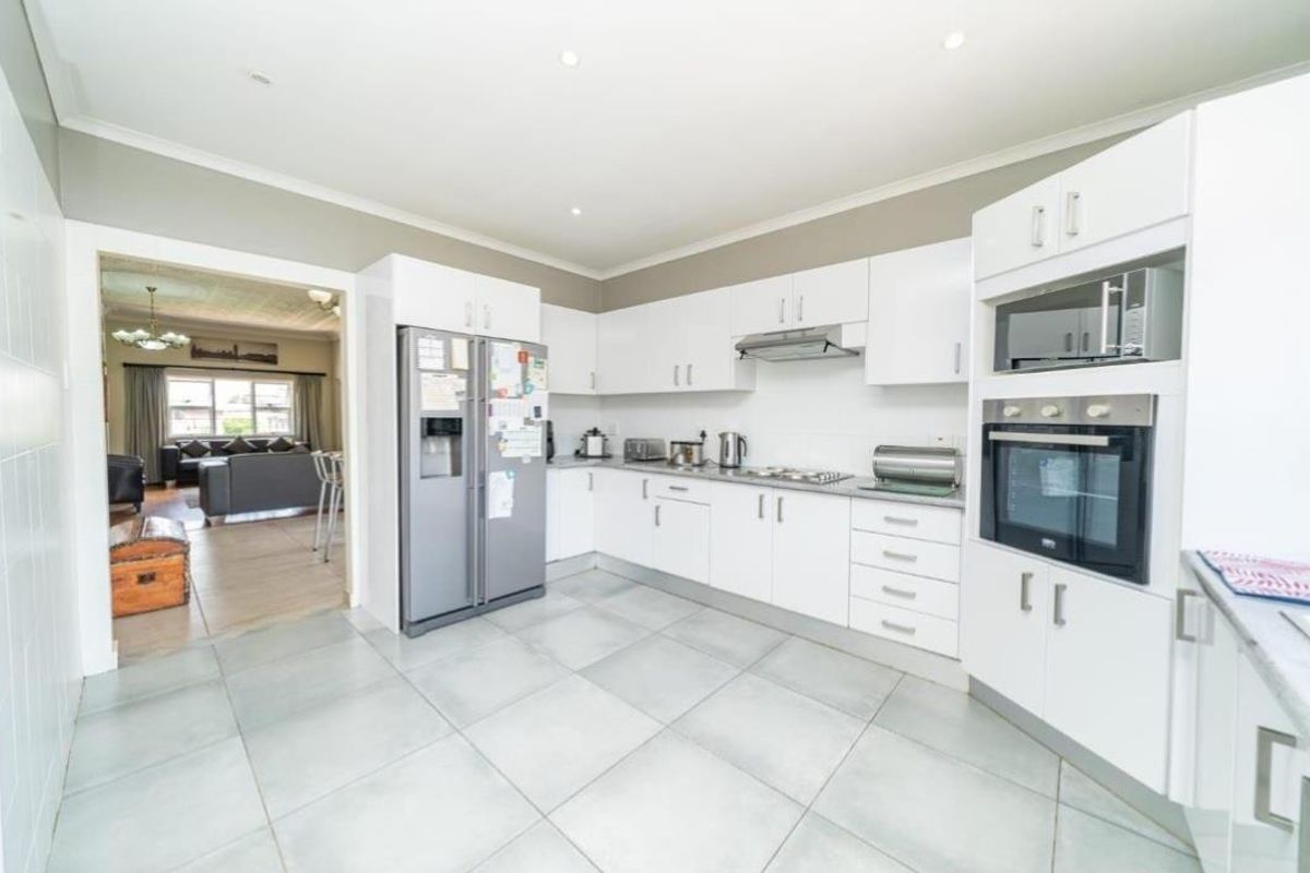 Modern kitchen featuring white cabinetry, built-in oven and microwave, extractor fan, and tiled flooring, with an open flow into the adjacent living area.