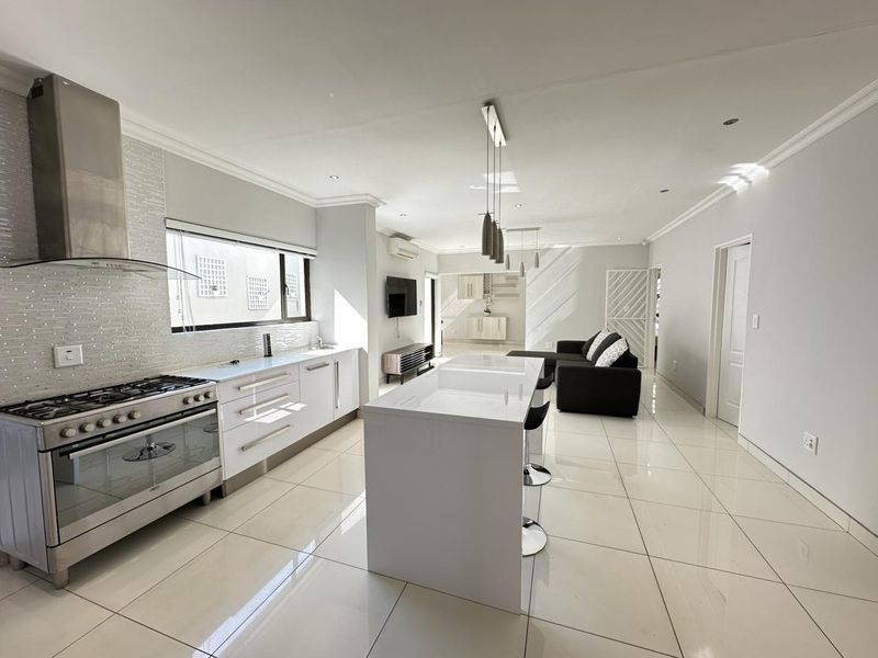 Modern open-plan living area featuring a sleek kitchen with a central island, gas stove, and high-gloss cabinetry, seamlessly flowing into the lounge space.