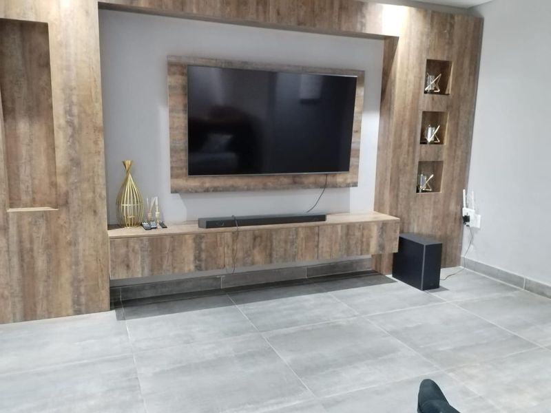 A modern living room featuring a custom built-in wooden media unit with integrated shelving and large format grey floor tiles.