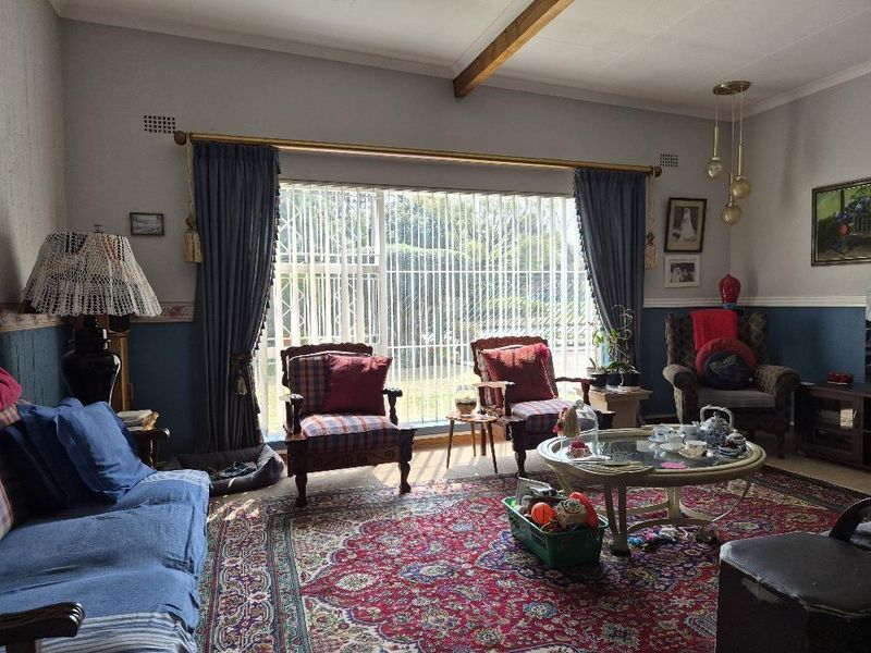 A traditional living room featuring an exposed timber ceiling beam, dado rail detailing, and a large sliding glass door with security gate access to outdoors.