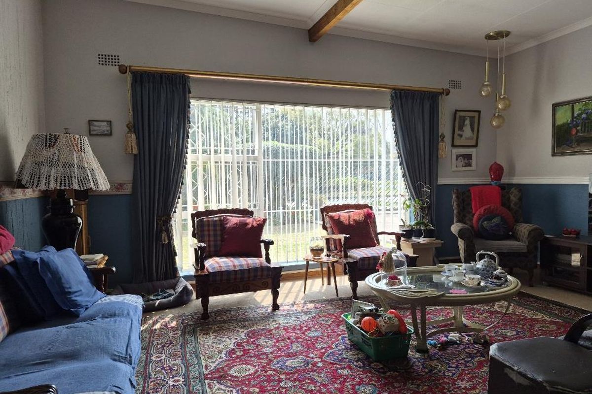 A traditional living room featuring an exposed timber ceiling beam, dado rail detailing, and a large sliding glass door with security gate access to outdoors.