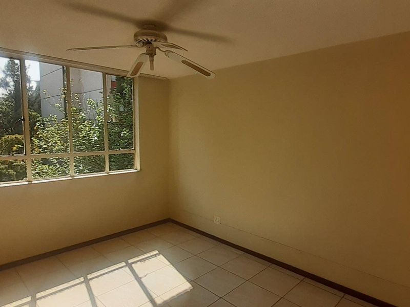 An empty bedroom featuring tiled flooring, a ceiling fan, and a large window providing natural light.
