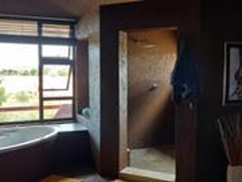 A spacious bathroom featuring a freestanding bathtub positioned by a large window, a walk-in shower, and earthy wall finishes.