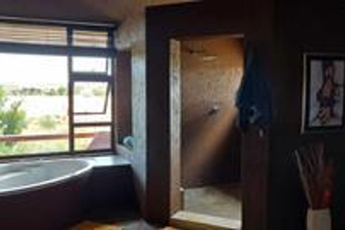 A spacious bathroom featuring a freestanding bathtub positioned by a large window, a walk-in shower, and earthy wall finishes.