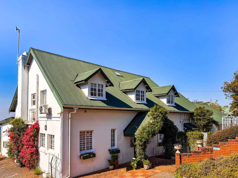 A charming multi-story building featuring a green corrugated metal roof, dormer windows, and a brick-paved entrance area with established landscaping.