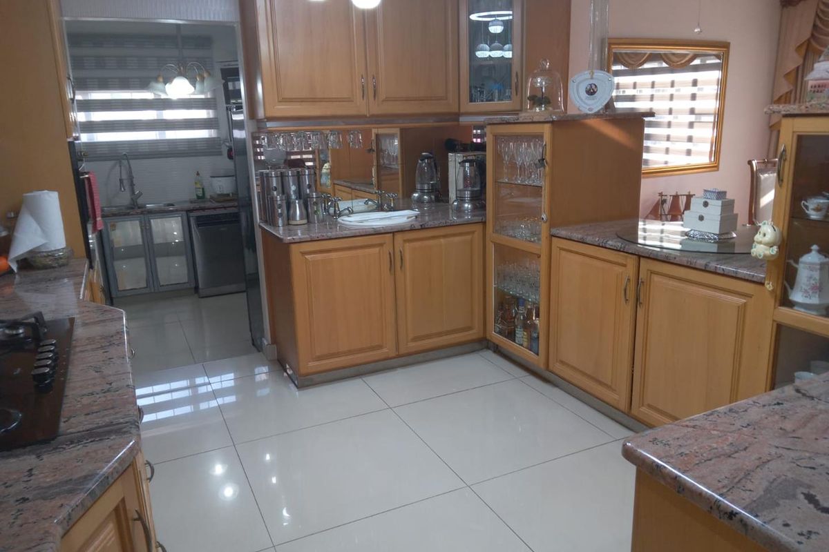 A functional kitchen featuring wooden cabinetry, granite countertops, and tiled flooring, with an adjacent scullery area visible through the doorway.