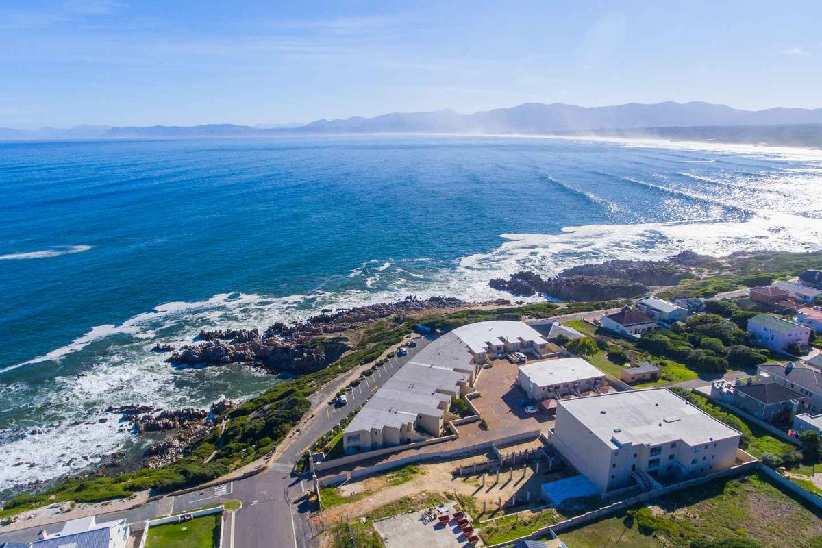 Aerial view of a coastal apartment complex situated directly along the shoreline, featuring paved parking and proximity to the ocean.