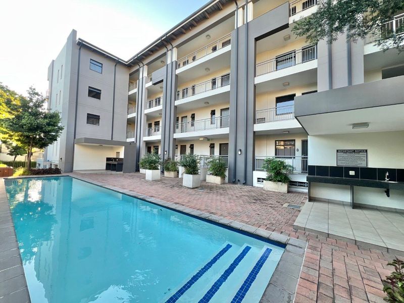 Communal apartment complex pool area featuring a paved deck, built-in outdoor counter, and multi-level balconies with metal railings.
