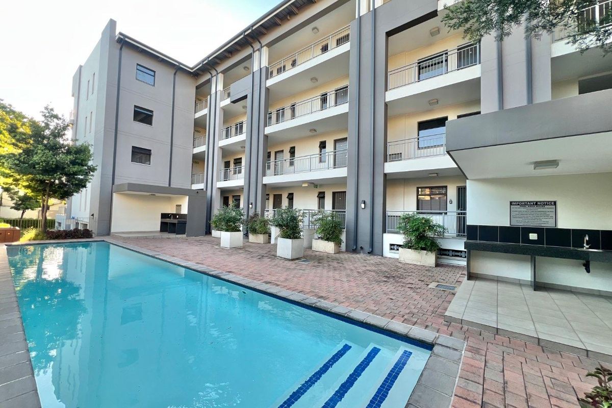 Communal apartment complex pool area featuring a paved deck, built-in outdoor counter, and multi-level balconies with metal railings.