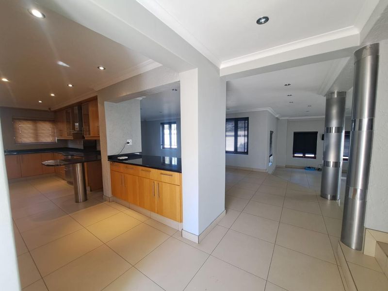 Spacious open-plan living and kitchen area featuring modern wooden cabinetry, granite countertops, neutral floor tiles, and recessed lighting throughout.