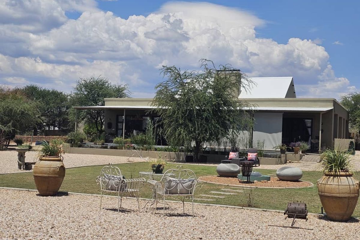 A well-maintained rear exterior view featuring a landscaped garden, gravel grounds, and a covered patio area attached to the main residence.