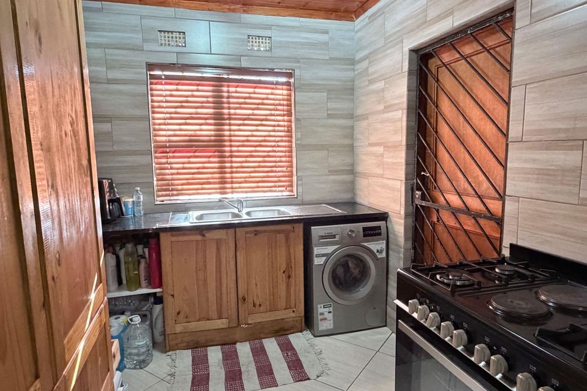 A functional kitchen featuring wooden cabinetry, tiled wall finishes, a double bowl sink, and a built-in stove with an extractor fan.