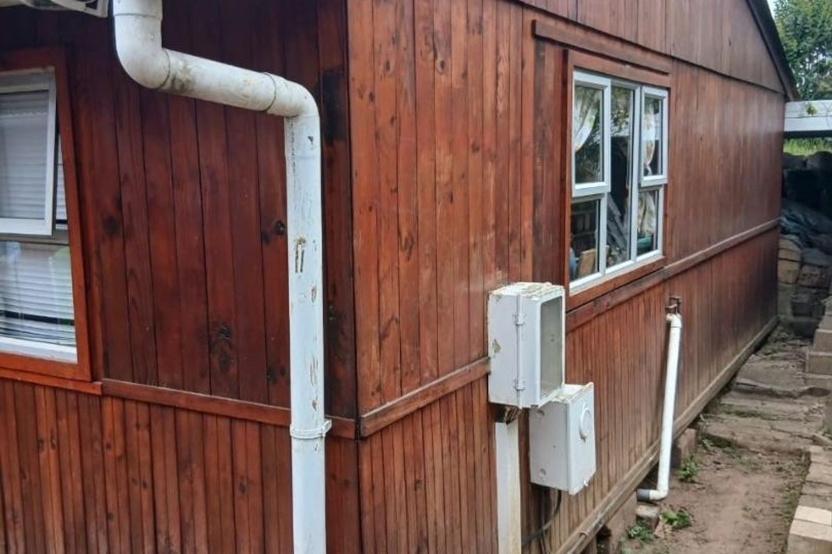 Exterior view of a timber-clad structure featuring corrugated roofing, PVC guttering, and casement windows, showing signs of weathering.