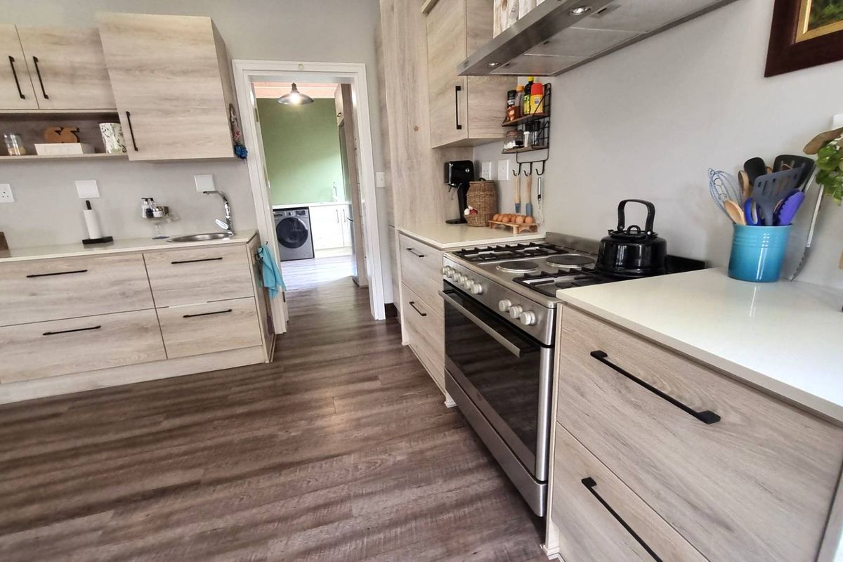 Modern kitchen featuring light wood-grain cabinetry, stone countertops, a gas stove with extractor fan, and durable laminate flooring, with an adjacent laundry area visible.
