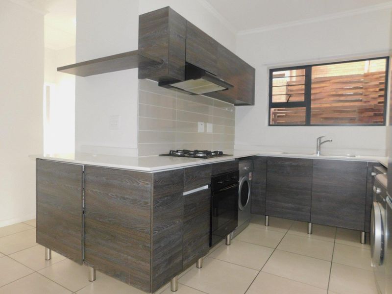Modern kitchen featuring dark wood-grain cabinetry, stone countertops, built-in oven, gas hob, extractor fan, and tiled flooring.