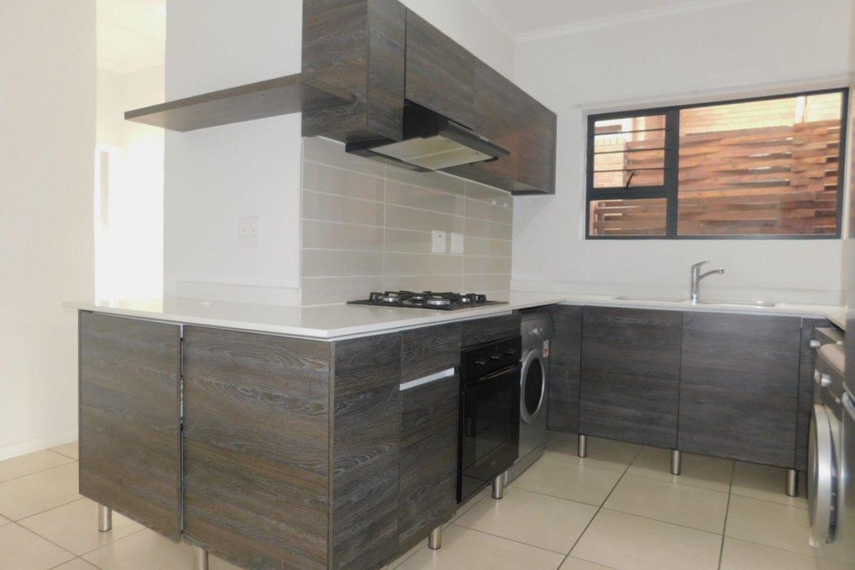 Modern kitchen featuring dark wood-grain cabinetry, stone countertops, built-in oven, gas hob, extractor fan, and tiled flooring.