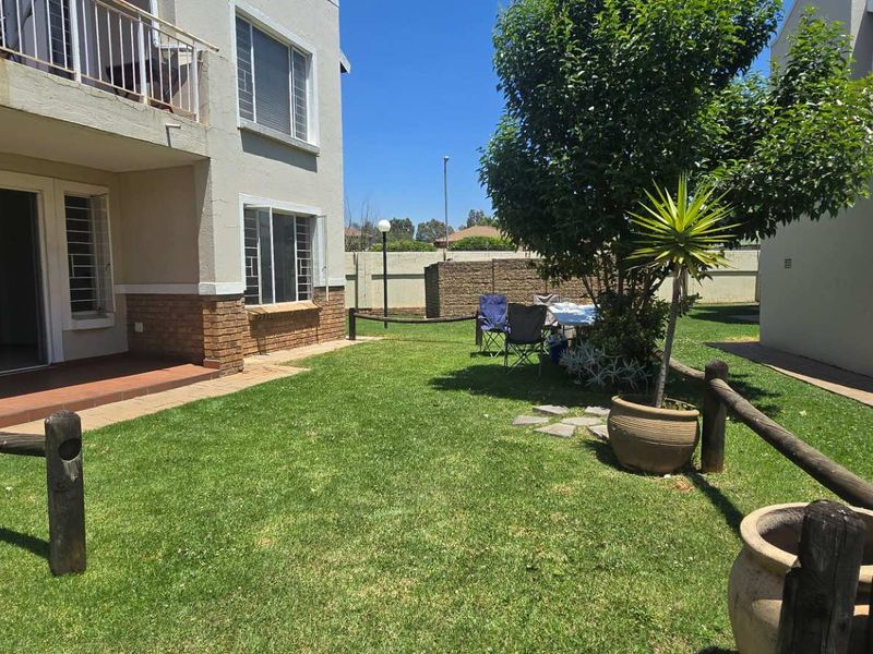 Rear view of the apartment building featuring a private garden, paved patio area, and a balcony with security bars.