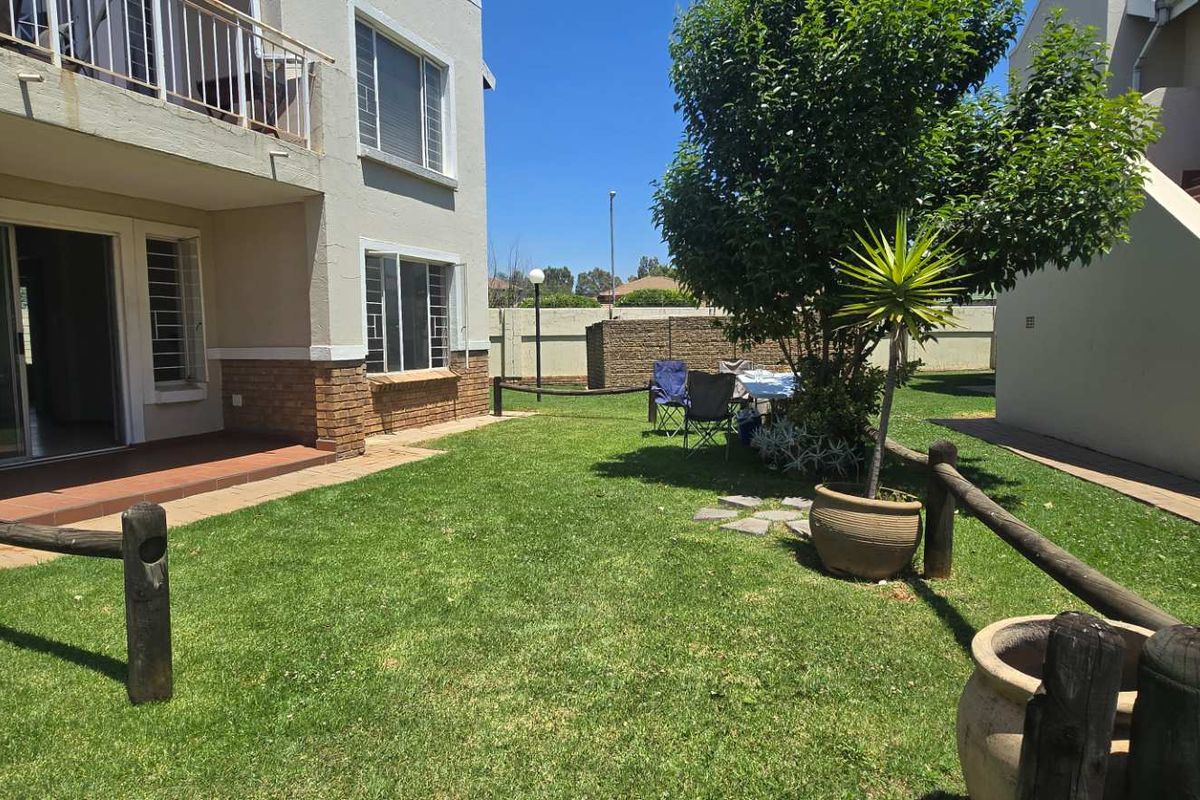 Rear view of the apartment building featuring a private garden, paved patio area, and a balcony with security bars.