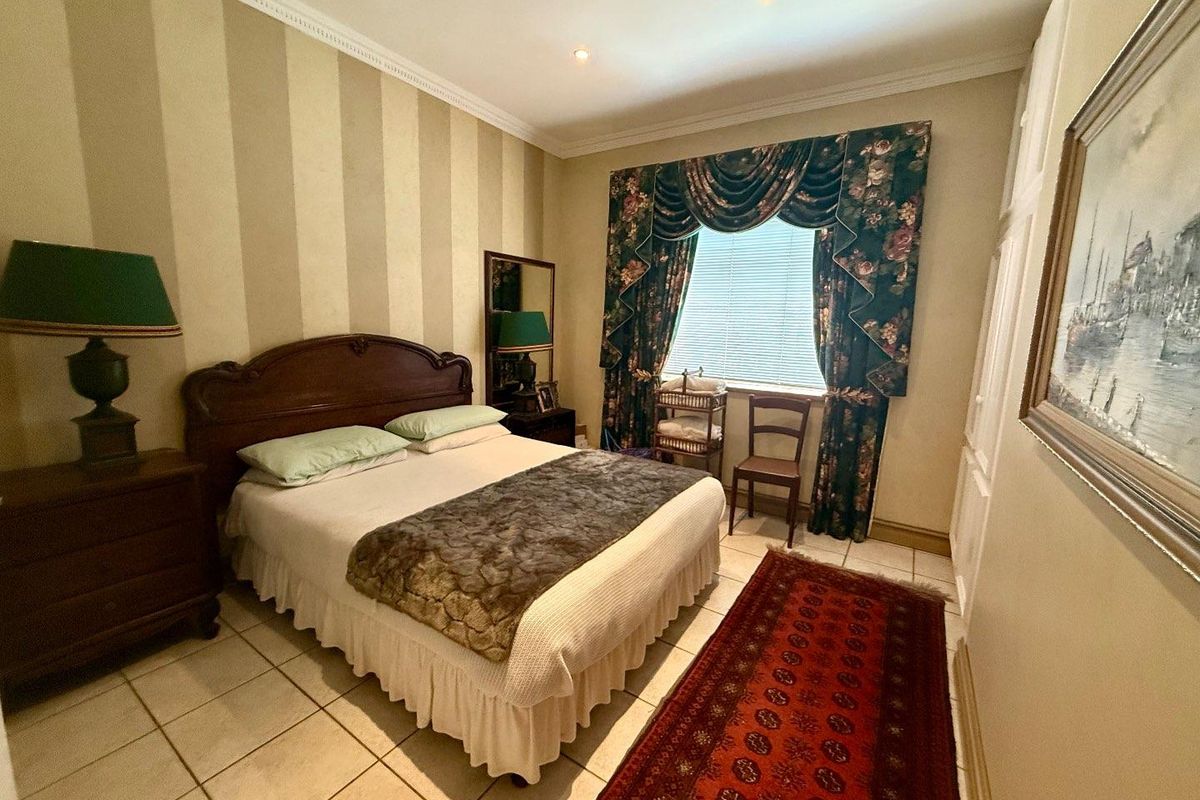 A bedroom featuring tiled flooring, crown molding, and built-in closet space, offering a functional layout with neutral striped wallpaper.