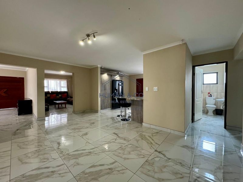 Spacious open-plan living area featuring polished marble-look floor tiles, a central breakfast bar, and seamless flow between the kitchen and adjacent living spaces.