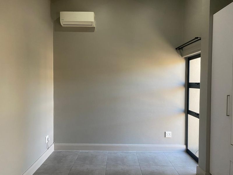 A clean, empty bedroom featuring neutral wall tones, tiled flooring, a built-in wardrobe, and a wall-mounted air conditioning unit.
