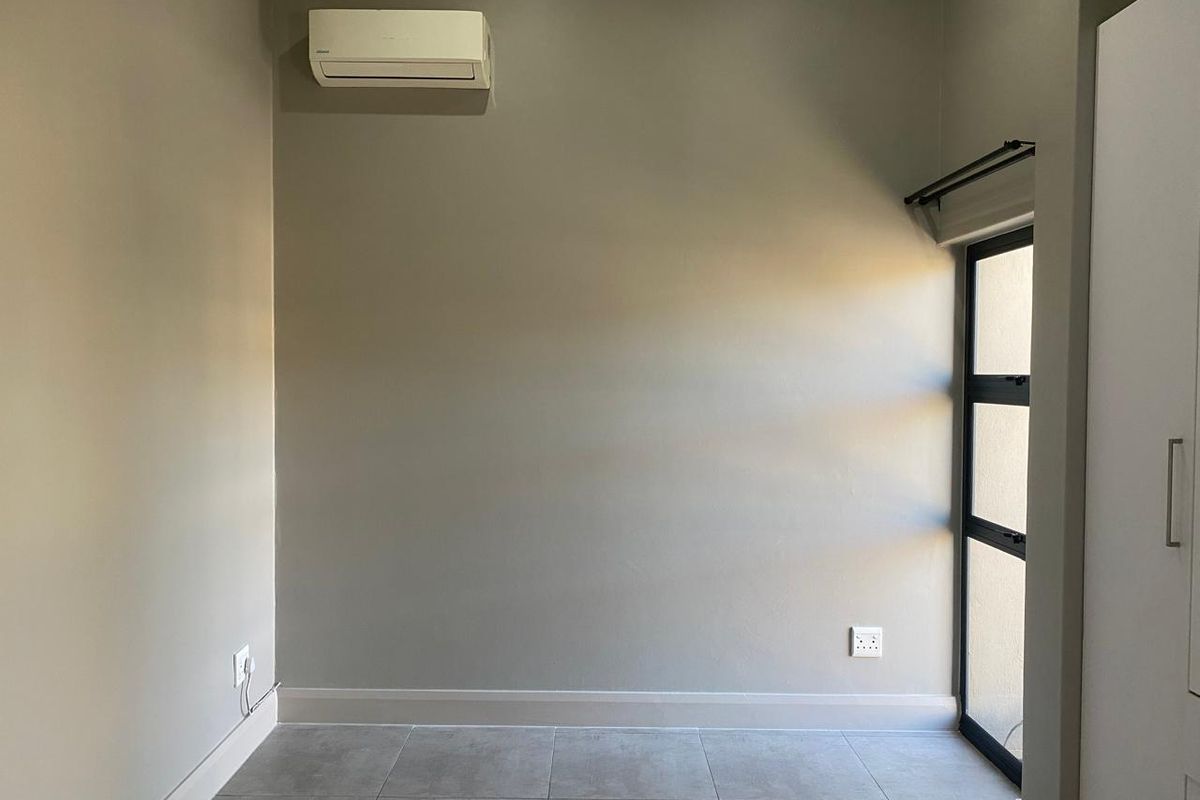 A clean, empty bedroom featuring neutral wall tones, tiled flooring, a built-in wardrobe, and a wall-mounted air conditioning unit.