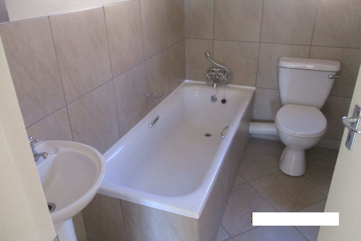 A functional bathroom featuring a pedestal basin, bathtub, and toilet with neutral wall and floor tiling.