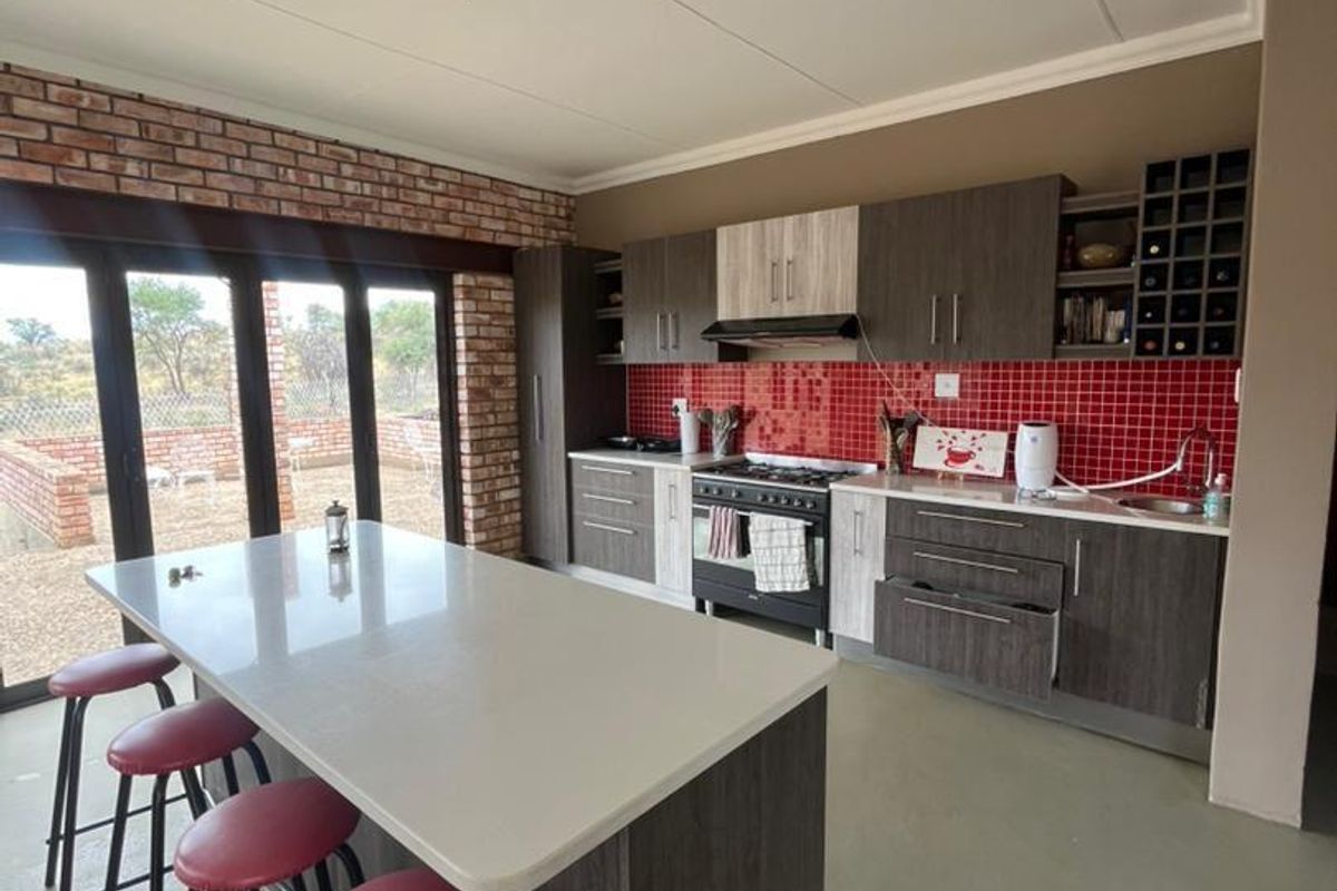 Modern kitchen featuring a central island, dark cabinetry, red tiled backsplash, and exposed brick accents, with direct access to the outdoor patio area.