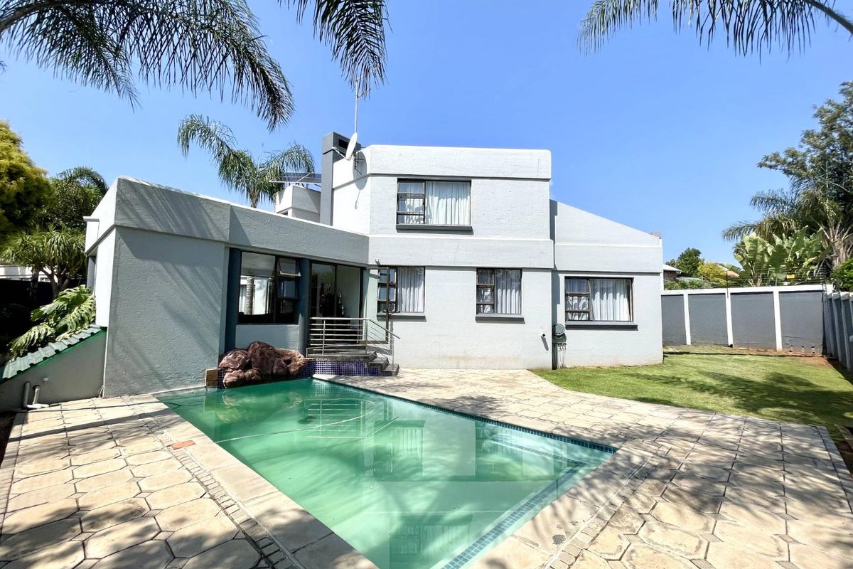 Rear view of the property featuring a swimming pool, paved patio area, and a well-maintained lawn with boundary walling.