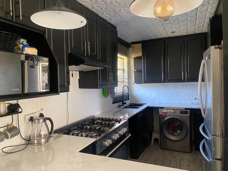 A compact kitchen featuring black cabinetry, stone countertops, a gas stove, integrated washing machine, and a distinctive textured ceiling finish.