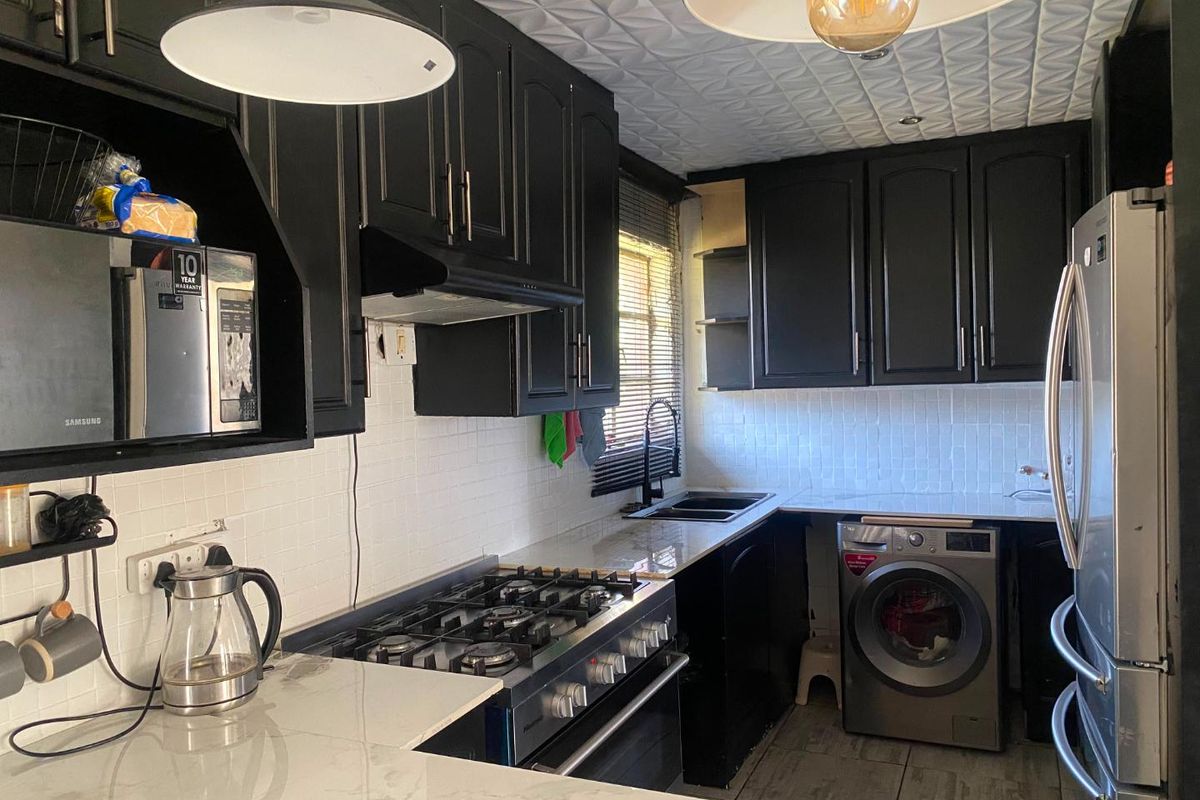 A compact kitchen featuring black cabinetry, stone countertops, a gas stove, integrated washing machine, and a distinctive textured ceiling finish.