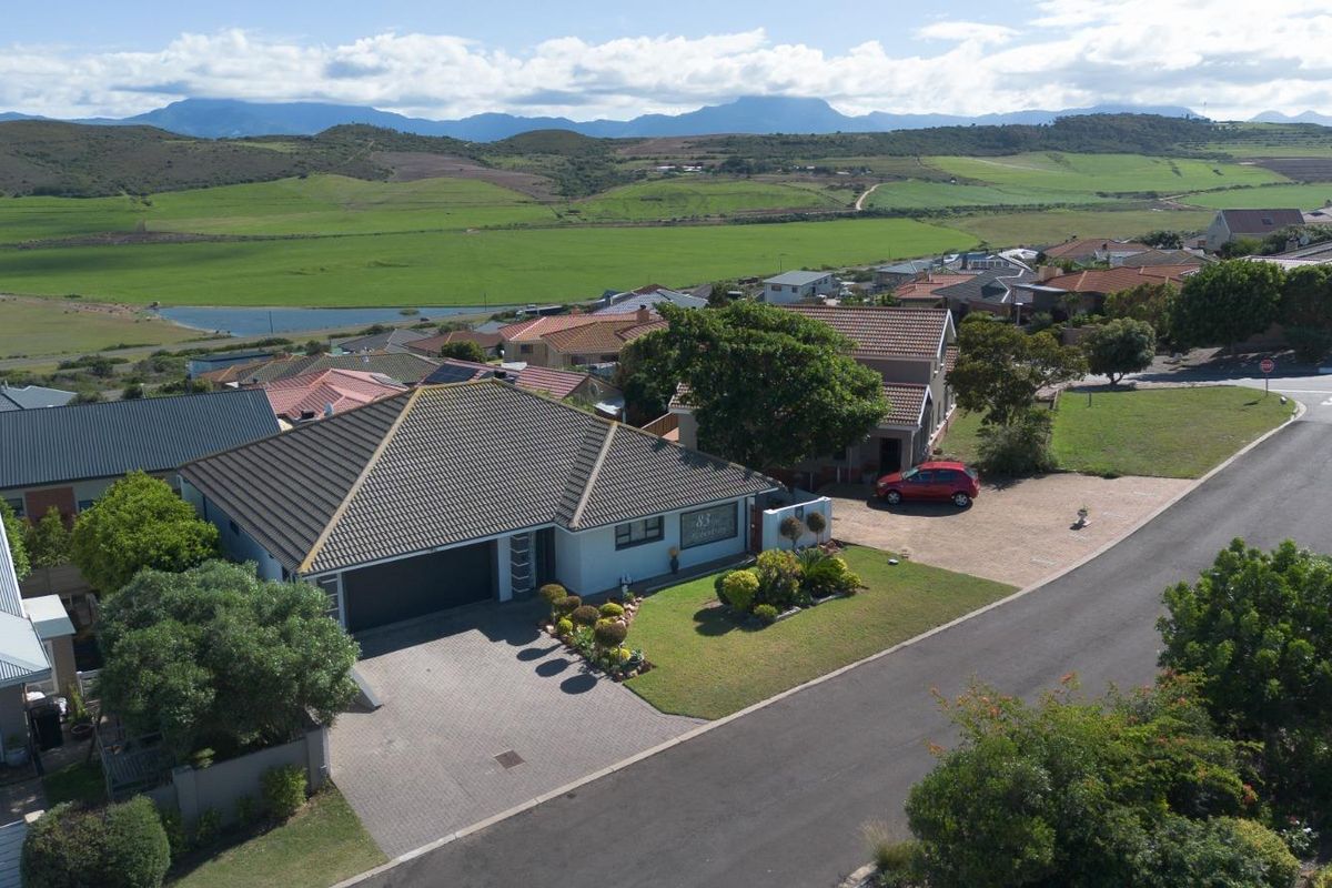 Aerial view of a residential property featuring a tiled roof, paved driveway, attached garage, and landscaped garden in a suburban setting.
